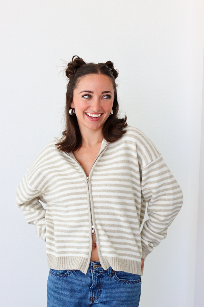 Woman wearing a tan and white striped zip-up sweater with blue denim jeans