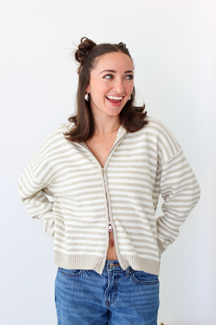 Woman wearing a tan and white striped zip-up sweater with blue denim jeans