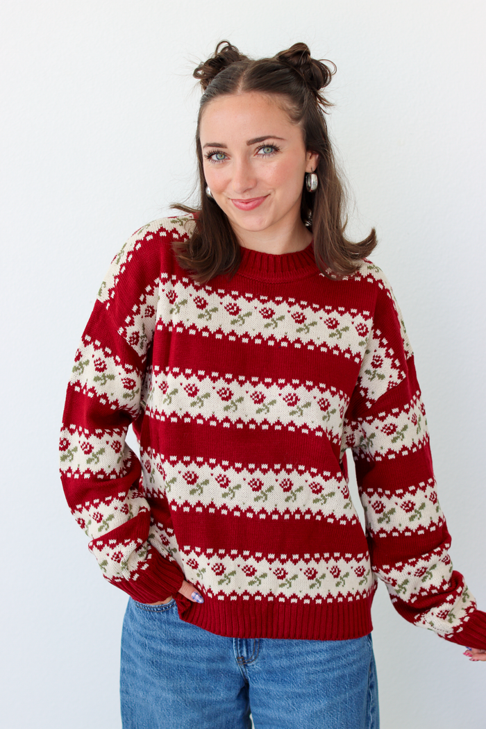 Woman wearing a red sweater with roses and blue denim jeans