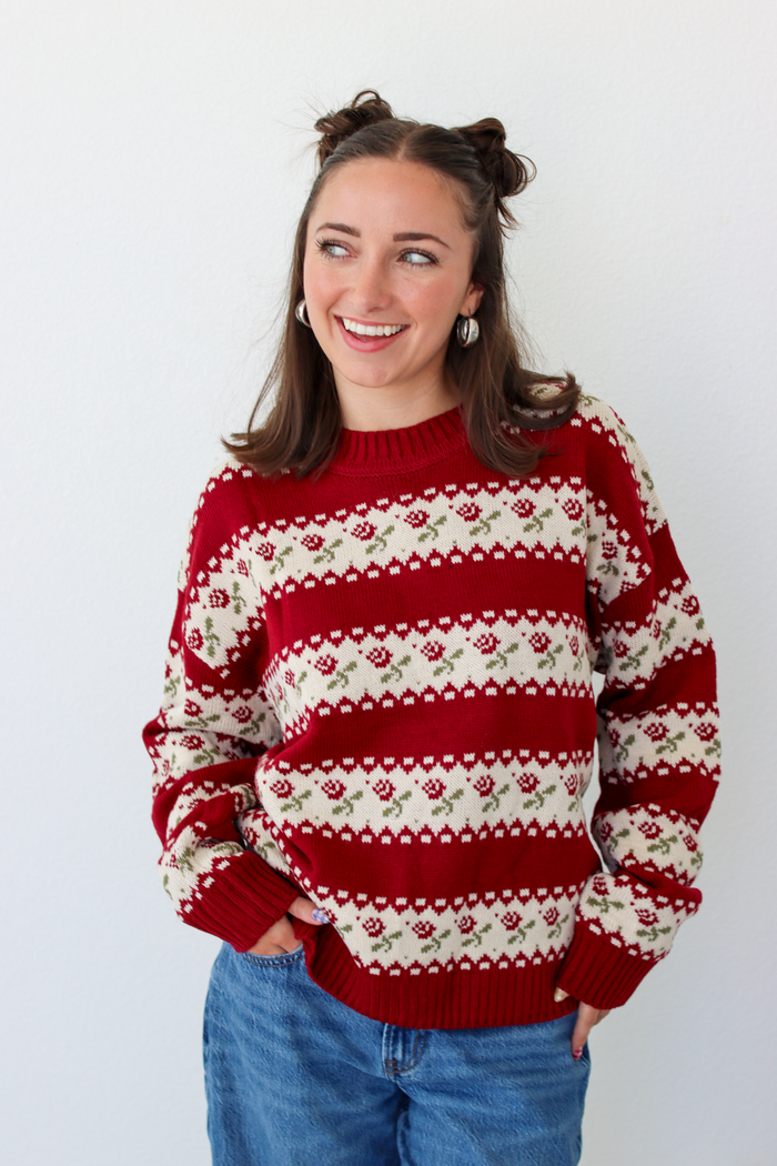 Woman wearing a red sweater with roses and blue denim jeans