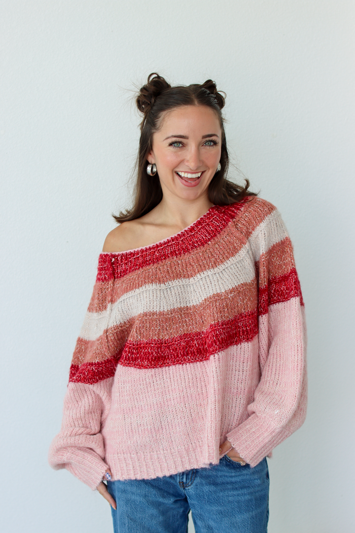 Woman wearing a pink stripe sweater off the shoulder with blue denim jeans