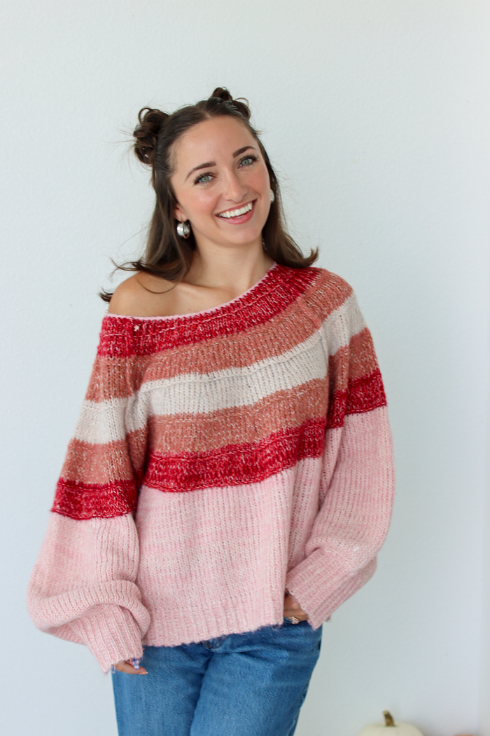 Woman wearing a pink stripe sweater off the shoulder with blue denim jeans
