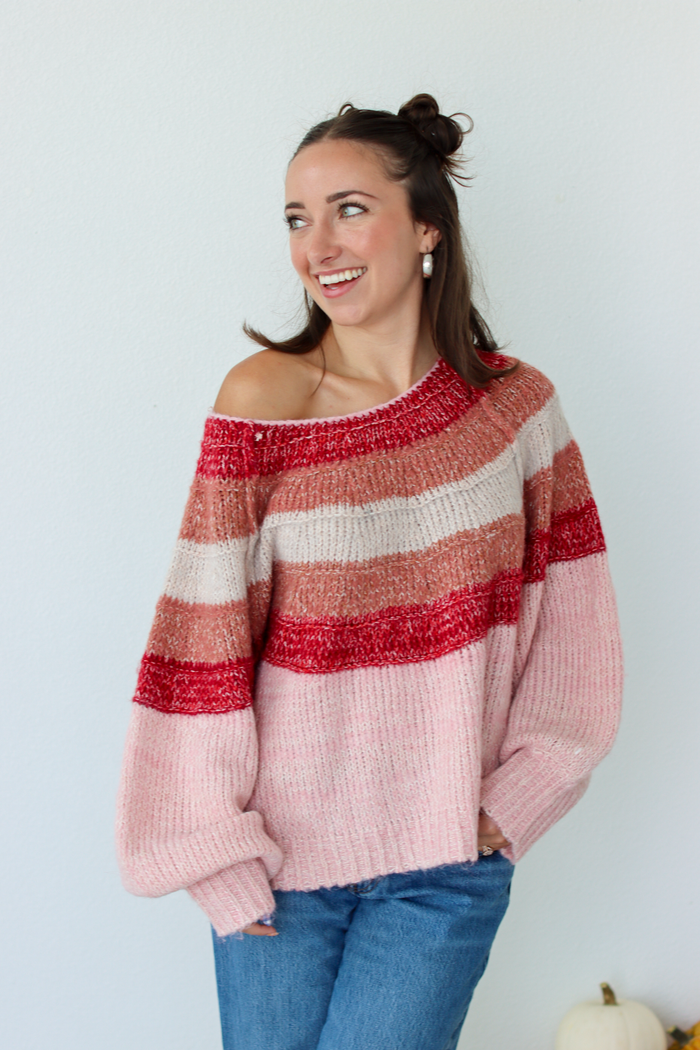Woman wearing a pink stripe sweater off the shoulder with blue denim jeans