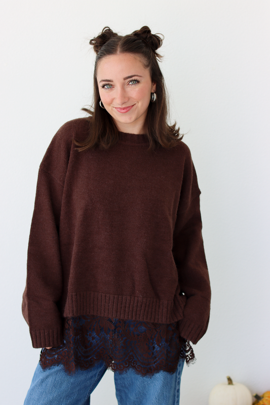 Woman wearing a brown sweater with lace trim detail at the bottom with blue denim jeans
