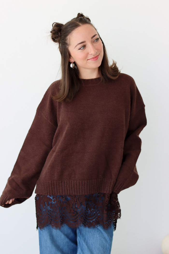 Woman wearing a brown sweater with lace trim detail at the bottom with blue denim jeans